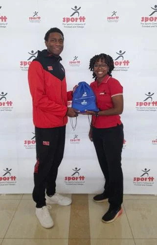 all smiles: Nikolai Blackman receives a branded token from Courtnee-Mae Clifford, the Sports Company of Trinidad and Tobago’s officer for aquatics, following a cheque handover to the local Aquatics Association.  —Photo courtesy SporTT (Image obtained via trindadexpress.com)